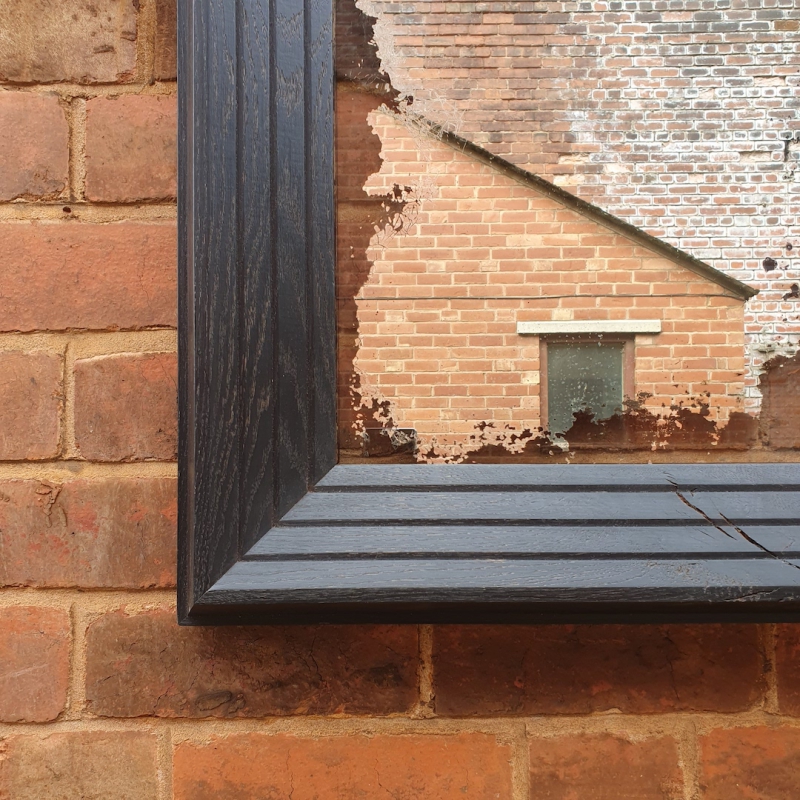 A corner close up of a reclaimed silver-backed mirror, preserved and framed in a hand-ebonised oak frame