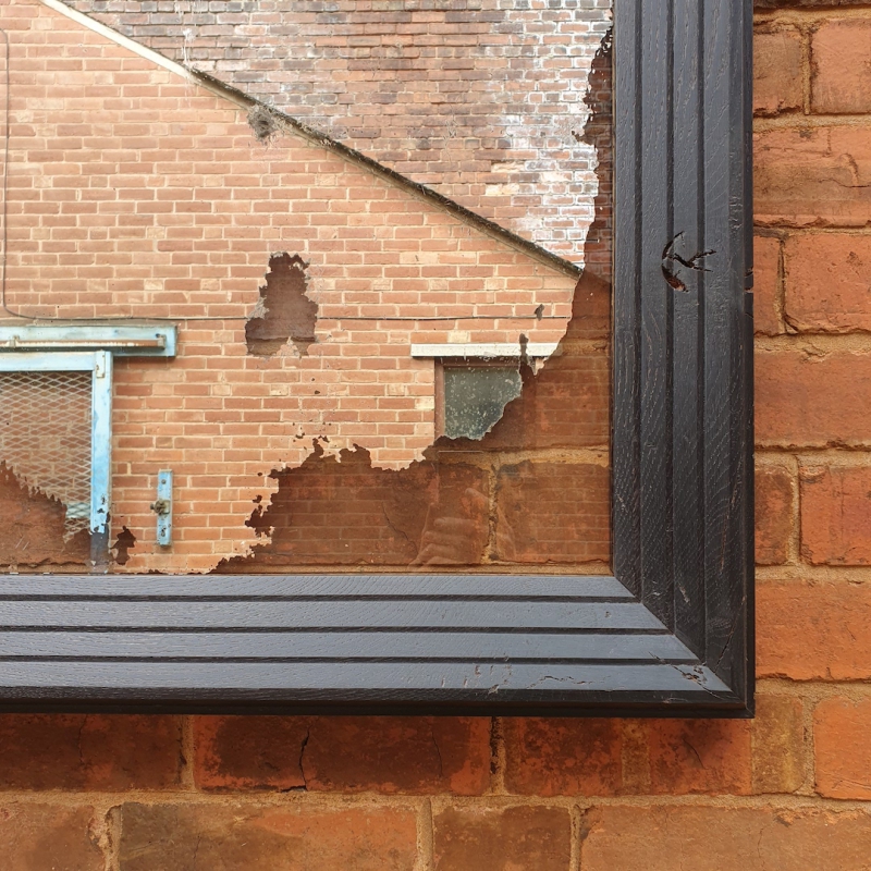 A corner close up of a reclaimed silver-backed mirror, preserved and framed in a hand-ebonised oak framee