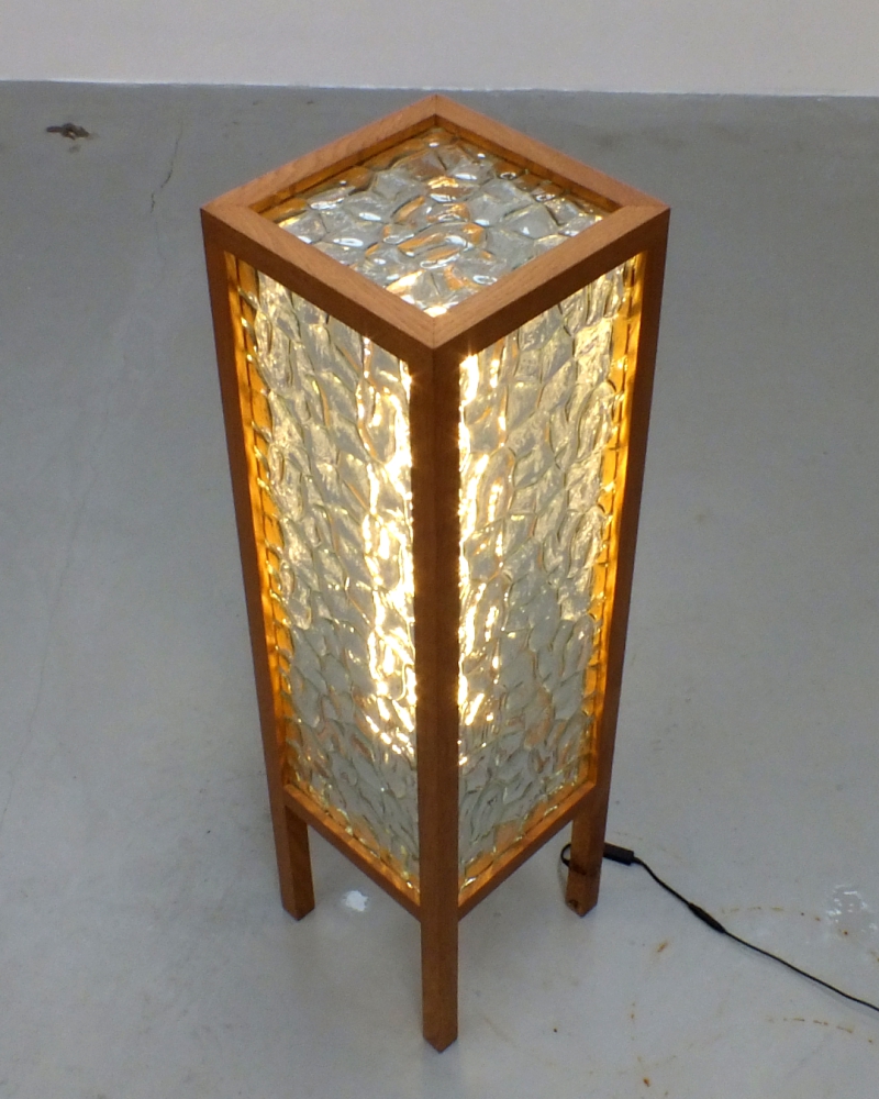 A handcrafted lamp made from reclaimed rippled glass and oak spindles