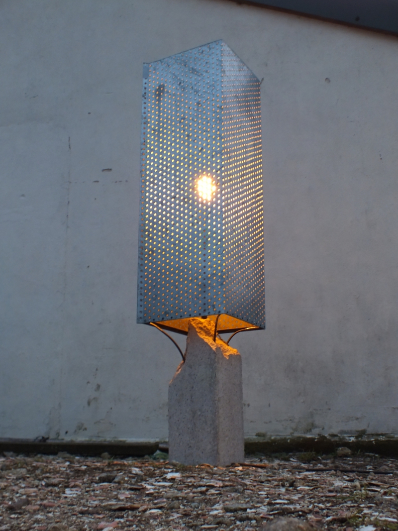 a dusk photo of a lamp made of concrete and perforated sheet steel